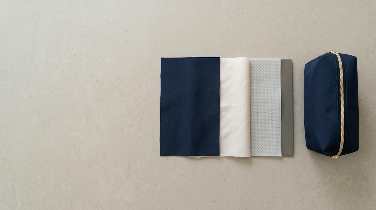 A cut cross-section of a cosmetic bag wall showing the outer shell fabric, a foam interlining layer and the inner lining, laid flat on a work table beside pattern pieces.