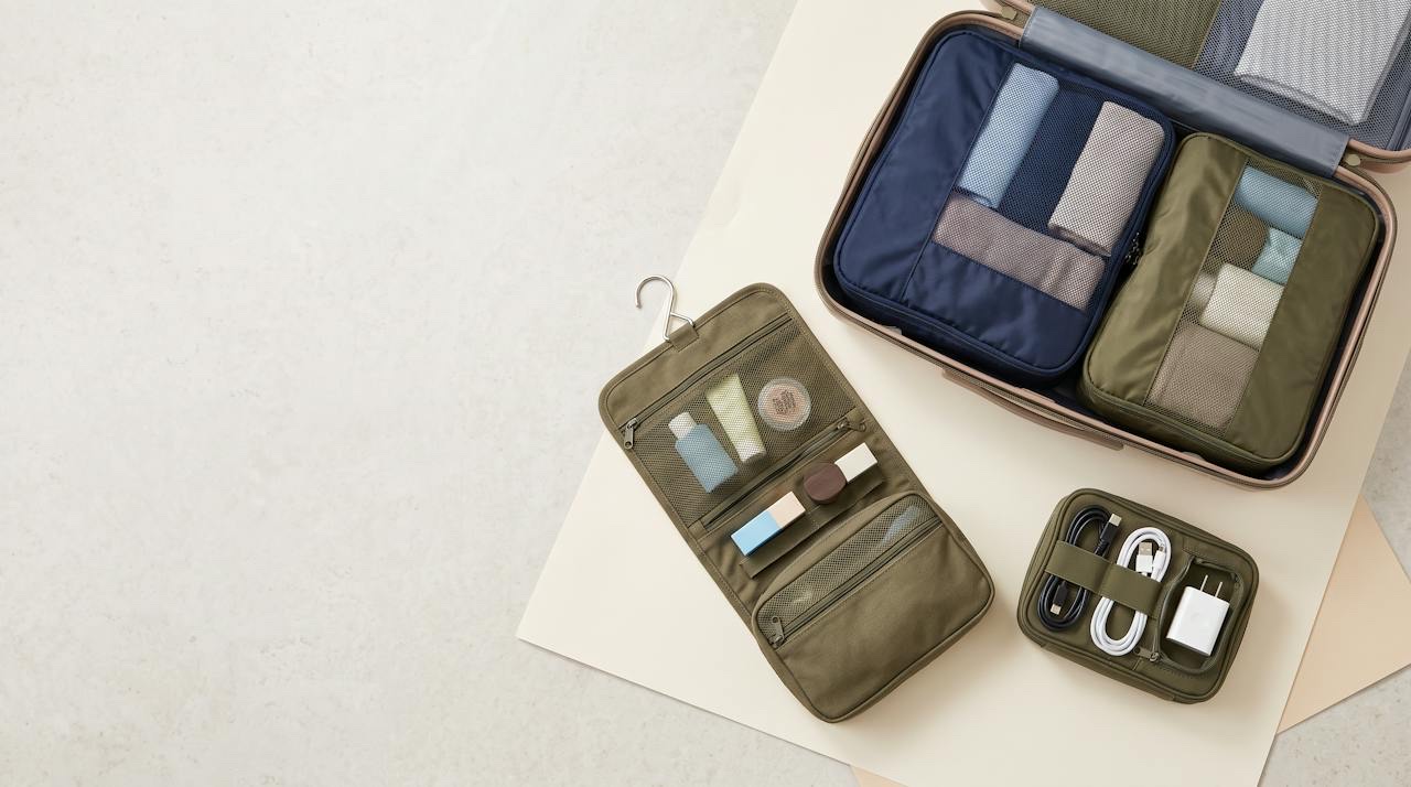 Colour-coded packing cubes, a hanging toiletry bag with a clear panel and a tech organizer with cable loops laid out beside an open suitcase